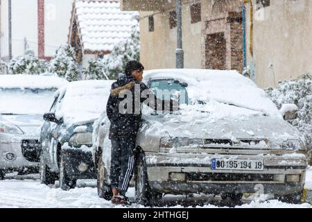 Vue à angle bas d'un garçon qui retire la neige d'une fenêtre de voiture. Banque D'Images