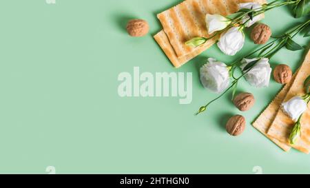 Concept de célébration de Pesah (fête de la Pâque juive), espace de copie. Pain matza traditionnel, noix, fleurs de printemps sur fond vert pastel. Banque D'Images