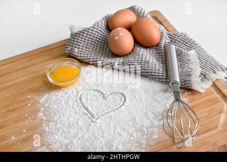 Planche en bois avec œufs de poulet, farine, coeur tiré et fouetter sur fond clair Banque D'Images