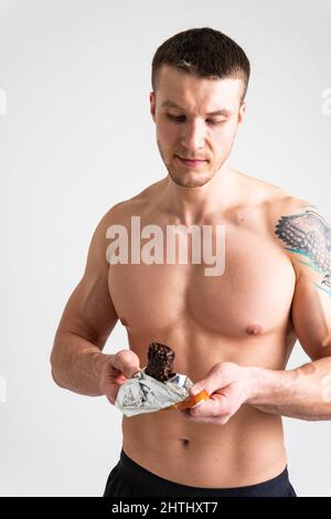 L'homme mange la barre de protéines sur fond blanc aliment de protéines isolé, goût athlète personne, entraînement de femme. Personnes en extérieur ABS, muesli femme Banque D'Images