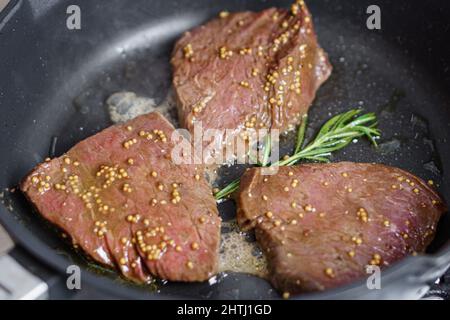 Rôtir les steaks de bœuf dans une poêle avec des graines de romarin et de moutarde en gros plan Banque D'Images