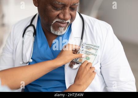 Main de femme noire mettant l'argent dans la poche du médecin Banque D'Images