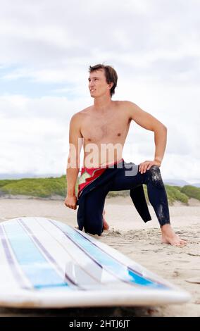 Préparation pour frapper les vagues. Un jeune surfeur s'étire sur la plage à côté de son conseil. Banque D'Images