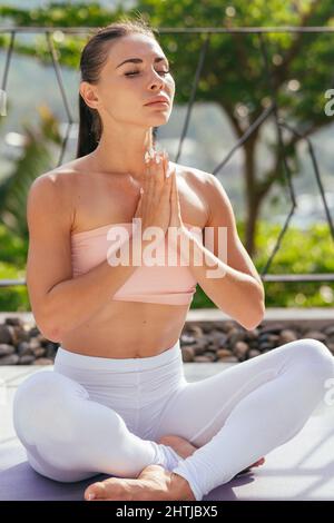 Jeune femme pratiquant le yoga, méditant dans la moitié de lotus poser avec namaste. Banque D'Images