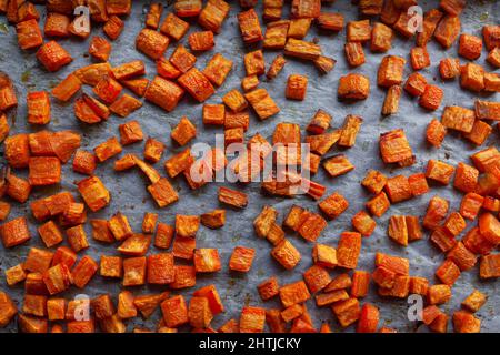 Cuire au four des carottes grillées et des patates douces sur un papier parchemin, coupé en cubes Banque D'Images