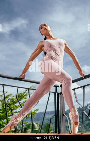 Ballerine jeune en pointes roses s'étirant, dansant sur les orteils en rayons chauds du soleil Banque D'Images