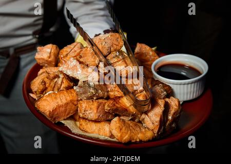 Un garçon tenant un grand plat avec des morceaux de saumon grillé. Gros plan, mise au point sélective Banque D'Images