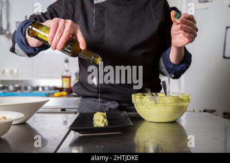 Un homme professionnel méconnaissable fait cuire de l'huile d'olive sur du guacamole vert tout en préparant un hors-d'œuvre dans la cuisine du restaurant Banque D'Images