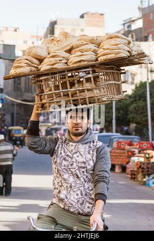 Le Caire, Égypte - 11 janvier 2022 : un homme ethnique livrant du pain pita égyptien à vélo dans la rue du Grand Bazar Banque D'Images