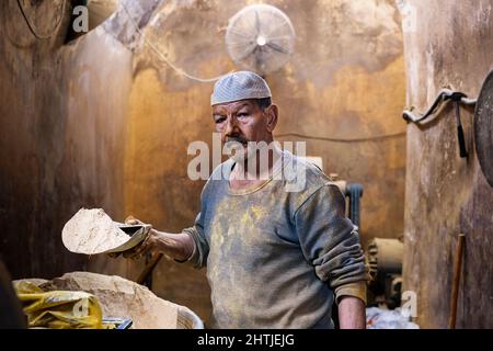 Le Caire, Egypte - 11 janvier 2022: Vendeur debout dans une petite cabine avec des murs de merde tout en montrant des épices de terre sur la pelle Banque D'Images