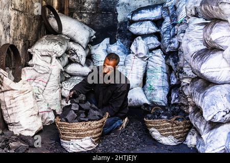 Le Caire, Egypte - 11 janvier 2022: Travailleur ethnique assis contre des sacs tout en collectant le charbon de bois dans des paniers pour la distribution aux clients Banque D'Images