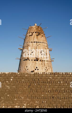 Tour de nidification d'oiseaux égyptiens haut conique avec trous et bâtons de bois situés près du mur de pierre contre ciel bleu sans nuages en Egypte Banque D'Images