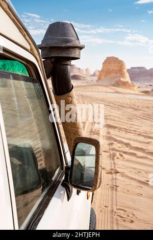 Voiture blanche garée sur un sol sablonneux près de formations rocheuses craies rugueuses situées dans la célèbre zone protégée du désert blanc en Égypte Banque D'Images