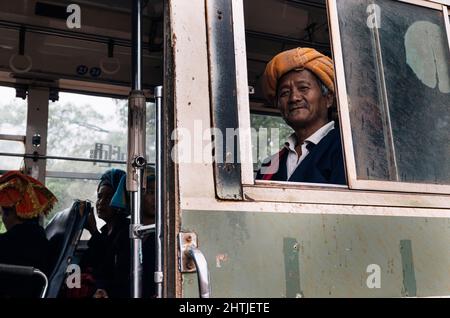 Kakku, Myanmar - 04.16.2017: Vieil homme asiatique de la minorité ethnique Karen avec une serviette traditionnelle turban près des passagers dans l'autobus Banque D'Images