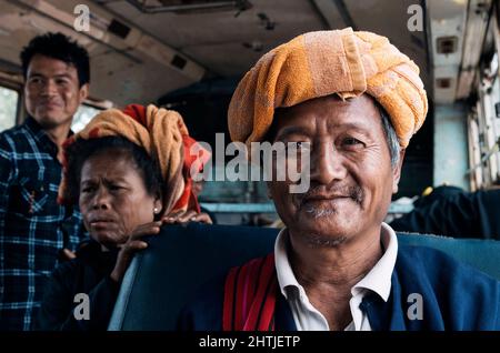 Kakku, Myanmar - 04.16.2017: Vieil homme asiatique de la minorité ethnique Karen avec une serviette traditionnelle turban près des passagers dans l'autobus Banque D'Images