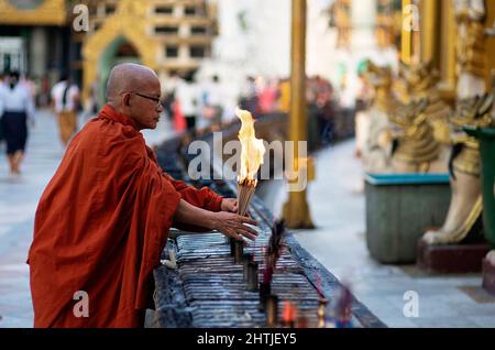 Yangon, Myanmar - 04.19.2017: Vue latérale d'un moine masculin ethnique âgé en robe avec bâtonnets d'encens brûlés dans la Pagode traditionnelle orientale du Shwedagon Banque D'Images