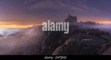 Château médiéval situé sur une falaise rocheuse agitée contre un ciel étoilé la nuit dans la nature avec de hauts arbres et du brouillard Banque D'Images