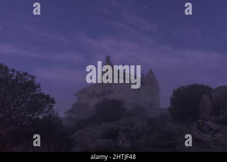 Château médiéval situé sur une falaise rocheuse agitée contre un ciel étoilé la nuit dans la nature avec de hauts arbres et du brouillard Banque D'Images