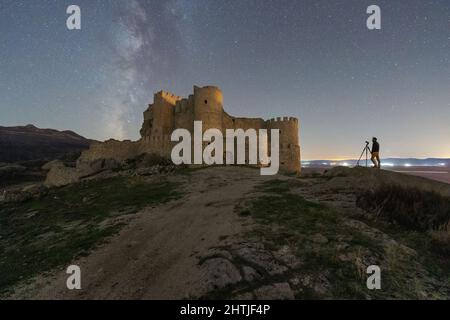 Vue latérale d'un photographe éloigné près de l'appareil photo sur un trépied debout près du château médiéval en pierre, la nuit, en campagne Banque D'Images