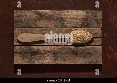 Vue de dessus cuillère en bois avec graines de sésame crues sur des planches en bois placées sur une table dans une pièce lumineuse Banque D'Images