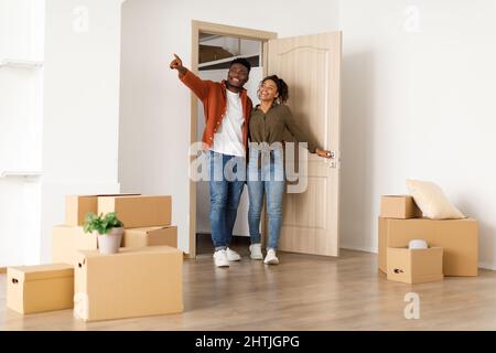 Les conjoints noirs excités entrent dans leur nouvelle maison, mari pointant de côté Banque D'Images