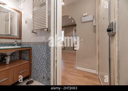 Salle de bains d'une maison avec carrelage en mosaïque avec armoire en merisier, comptoir en verre et évier en porcelaine blanche Banque D'Images