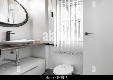 Petite salle de bains avec comptoir en marbre, évier en porcelaine sans insert, drainpipe en acier et miroir rond avec cadre noir Banque D'Images