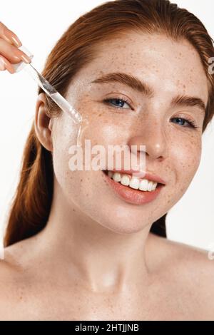 Belle femme de taille plus appliquer du sérum hydratant pour le visage sur fond blanc. Procédures quotidiennes de luxe de beauté le matin. Soin et rajeunissement de la peau Banque D'Images