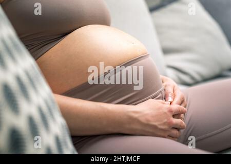 Femme enceinte ventre. Concept de grossesse. Ventre de la femme enceinte en gros plan. Détail de la femme enceinte se relaxant sur un canapé confortable à la maison. Banque D'Images