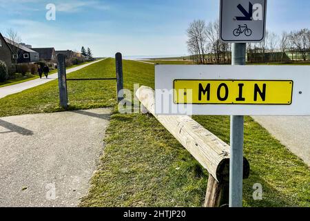 01 mars 2022, Schleswig-Holstein, Brunsbüttel: Deux personnes marchent le long d'une digue par temps ensoleillé et passent un panneau indiquant "mon". Photo: Frank Molter/dpa Banque D'Images