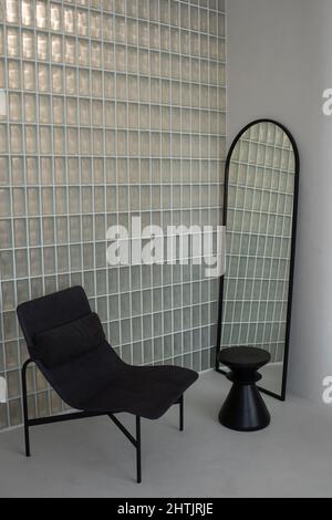 Coin de la chambre dans un appartement spacieux et contemporain avec chaise confortable, miroir en forme de arche et petite table noire Banque D'Images