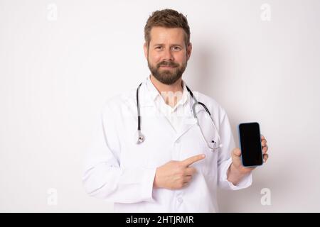 Jeune homme souriant médecin montrant écran téléphone portable isolé sur fond blanc. Concept médical. Banque D'Images
