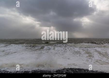 Les rayons du soleil de derrière les nuages brillent sur les vagues de turbulence pendant la tempête intense Eunice sur la côte à Vlissingen, pays-Bas Banque D'Images