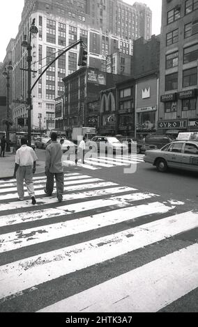 1980s, historique, deux hommes sur un passage de côté marqué sur West 33rd St près du grand magasin Macy's, Midtown, Manhattan, New York City, NY, ÉTATS-UNIS. À New York, les piétons ont un droit de passage dans tous les passages pour piétons, y compris les insections, que le passage pour piétons soit marqué ou non. Une promenade en croix ou un passage piéton a été introduit pour la première fois en 1951 à Slough, en Angleterre, au Royaume-Uni, où en raison de ses rayures est devenu connu comme un passage à zébré. Banque D'Images