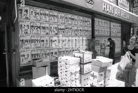 1980s, historique, extérieur du supermarché asiatique d'origine Han Ah REUM, Woodside, Queens, New York City, NY, États-Unis, montrant la fenêtre du magasin entièrement recouverte d'autocollants de vente et avec des boîtes de nourriture empilées sur la chaussée à l'extérieur, y compris des boîtes de Cantalopupes et de Nashi de Nouvelle-Zélande. En 1982, il Yeon Kwon a ouvert le premier magasin d'alimentation Han Ah Reum à Queens, NY, qui devint plus tard une grande chaîne de supermarchés asiatiques ou coréens-américains, connus sous le nom de H. Mart. Banque D'Images