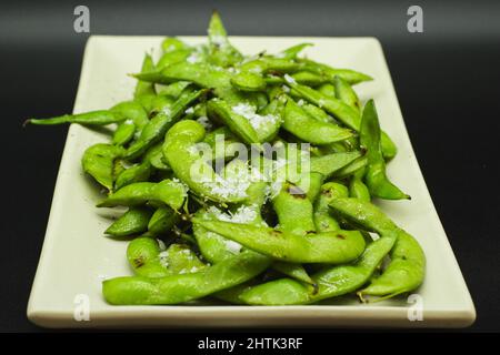 Portion d'Edamame vert cuit et salé prêt à manger, apéritif japonais sain sur fond noir. Banque D'Images