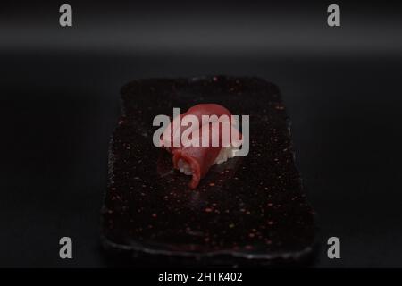 Deux unités de nigiris de thon rouge frais et traditionnel servies dans une assiette noire sur fond noir par un chef de restaurant japonais. Banque D'Images