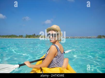 Pagayer vers la plage. Une belle jeune femme pagayant sur un bateau dans un océan tropical. Banque D'Images