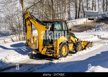 Travaux de déneigement, machine de déneigement en action par temps froid d'hiver. Un gros tracteur orange nettoie la neige de la route Banque D'Images