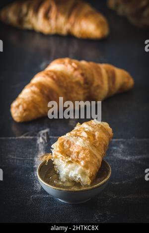 Morceau de délicieux croissant français plongé dans de la confiture, fond noir, vertical Banque D'Images