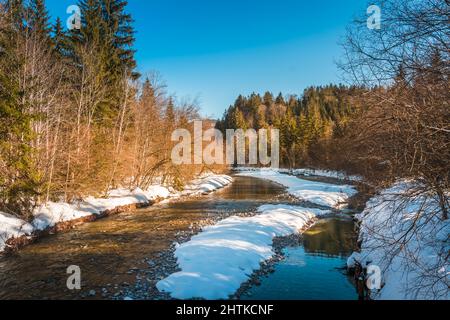 Paysage neigeux avec une crique partiellement gelée dans les Alpes lors d'un après-midi d'hiver ensoleillé Banque D'Images