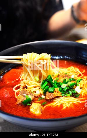 Croque-bettes de noddle de soupe chinoise de nouilles de bœuf à la tomate, nappées d'oignons verts de printemps. Banque D'Images