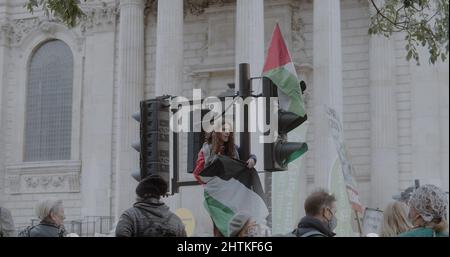 Londres, Royaume-Uni - 11 06 2021 : une jeune militante palestinienne a drapé un drapeau, se tenant au feu de circulation à St Paul’s Churchyard, pour COP26. Banque D'Images