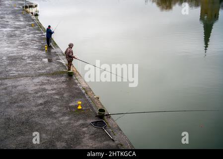 Pêcheurs sur le bord de la rivière en face d'une église Banque D'Images