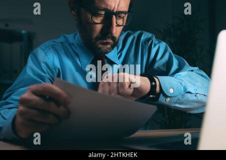 Travaillant tard dans la nuit, homme d'affaires dans l'intérieur sombre de bureau regardant sa montre-bracelet, foyer sélectif Banque D'Images