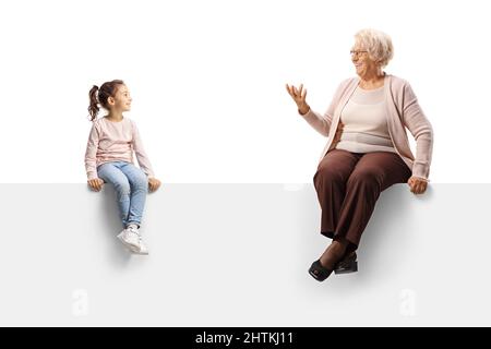 Femme âgée assise sur un panneau vierge et parlant à une petite fille isolée sur fond blanc Banque D'Images