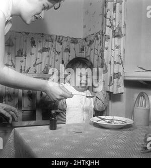 Garçon dans les 1950s. Un petit garçon en colère est nourri à la cuillère de sa nourriture contre sa volonté. Il semble contrarié et en colère et n'est pas prêt à manger plus. La mère toujours positive et souriante fait de son mieux pour le faire. Suède 1951 Kristoffersson Banque D'Images