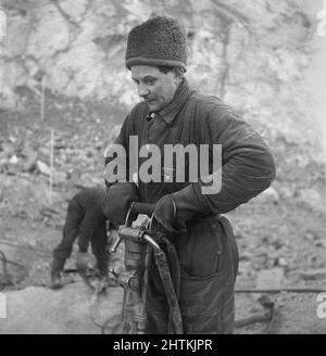 Kiruna Suède en 1950s. La mine à ciel ouvert et les ouvriers forant des trous pour y mettre des explosifs. Le semoir est alimenté par de l'air comprimé et le bruit aurait été très élevé mais l'homme qui travaille avec lui semble ne pas remarquer le son, même sans porter de protection auditive. Il a peut-être déjà eu une telle mauvaise audition que le problème de la haute noice n'est pas un problème. Suède 1954 Kristoffersson BP22-11 Banque D'Images