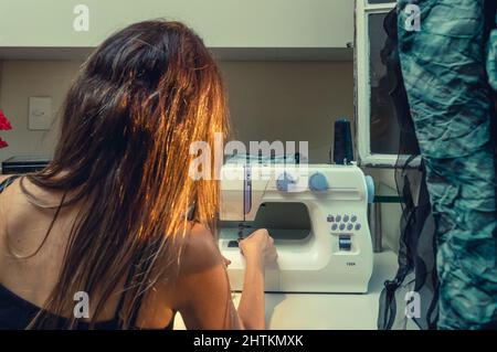 vue arrière d'une femme filant un fil bleu foncé dans l'aiguille de sa machine à coudre, dans son atelier de couture. concept textile. Banque D'Images