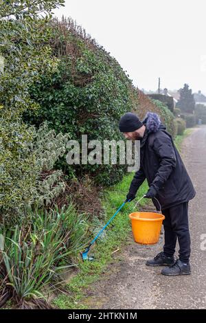 Un jeune barbu avec un préparateur de litière et un seau pour recueillir la litière et les ordures d'une ruelle de campagne. Collecte de litière, déchets, concept environnemental Banque D'Images